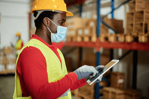 A person with a hard hat and looking at a tablet in a warehouse